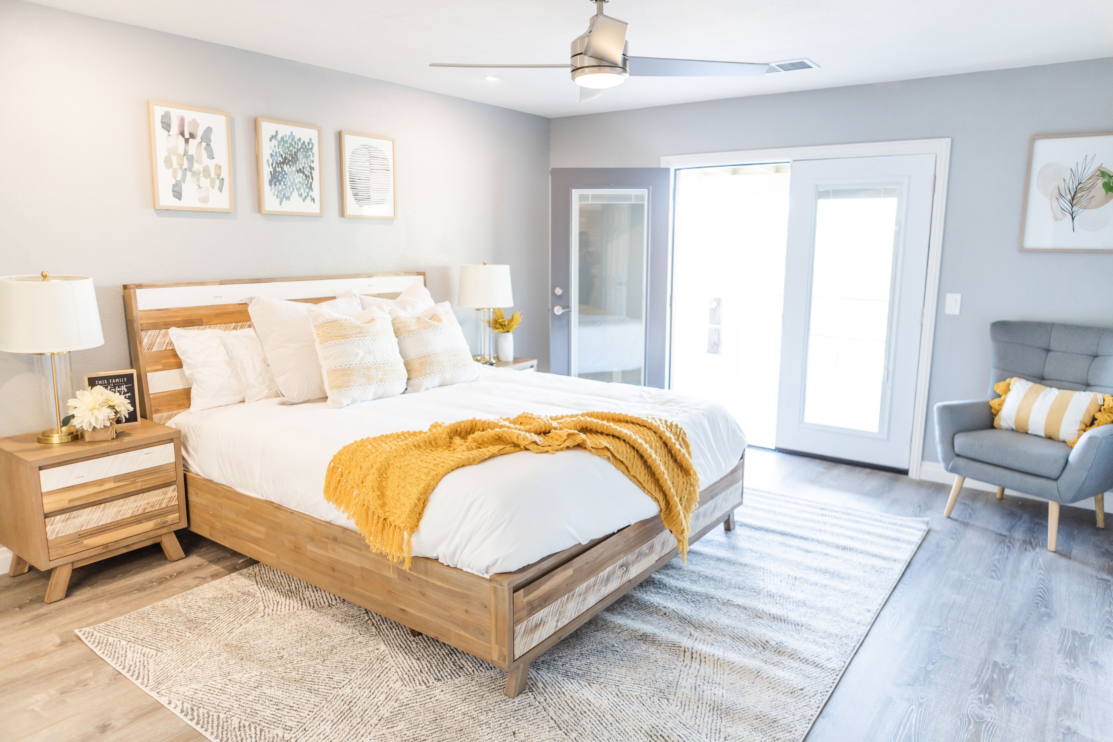Une chambre avec un lit en bois, des tables de chevet, un ventilateur de plafond et une vue sur l’extérieur grâce à une porte-fenêtre coulissante.