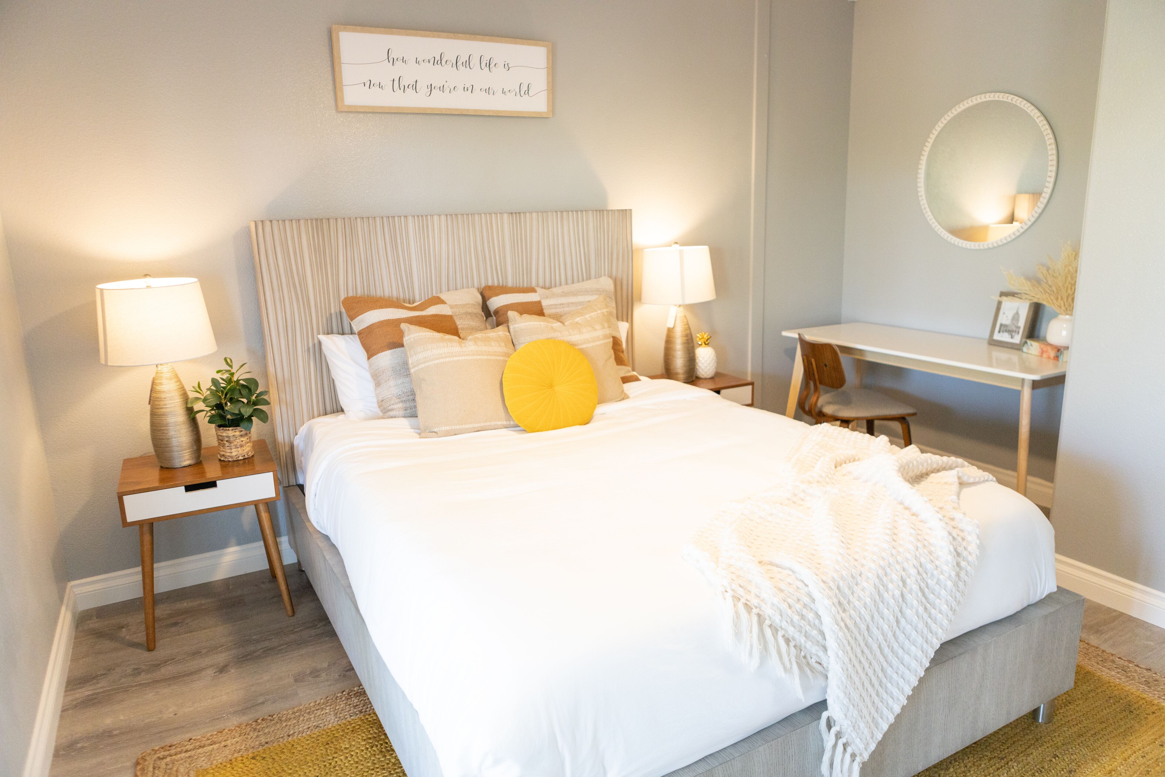 A bedroom with a bed, bedside tables, a desk, a mirror, and a wall-mounted sign.
