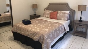 Una cama bien hecha con colcha floral, cabecera y dos mesitas de noche con lámparas.