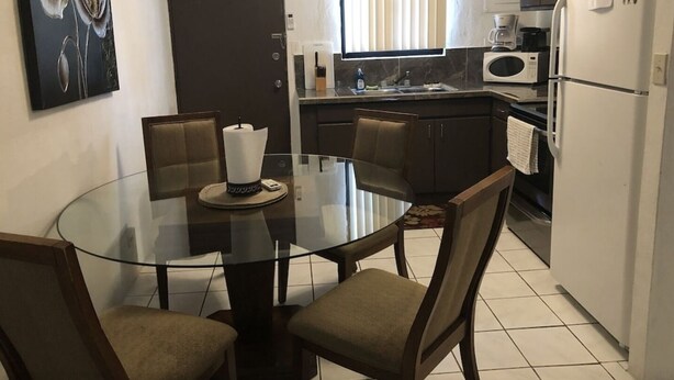 Una cocina moderna con una mesa de comedor de vidrio, sillas de madera oscura, un refrigerador blanco y un microondas.