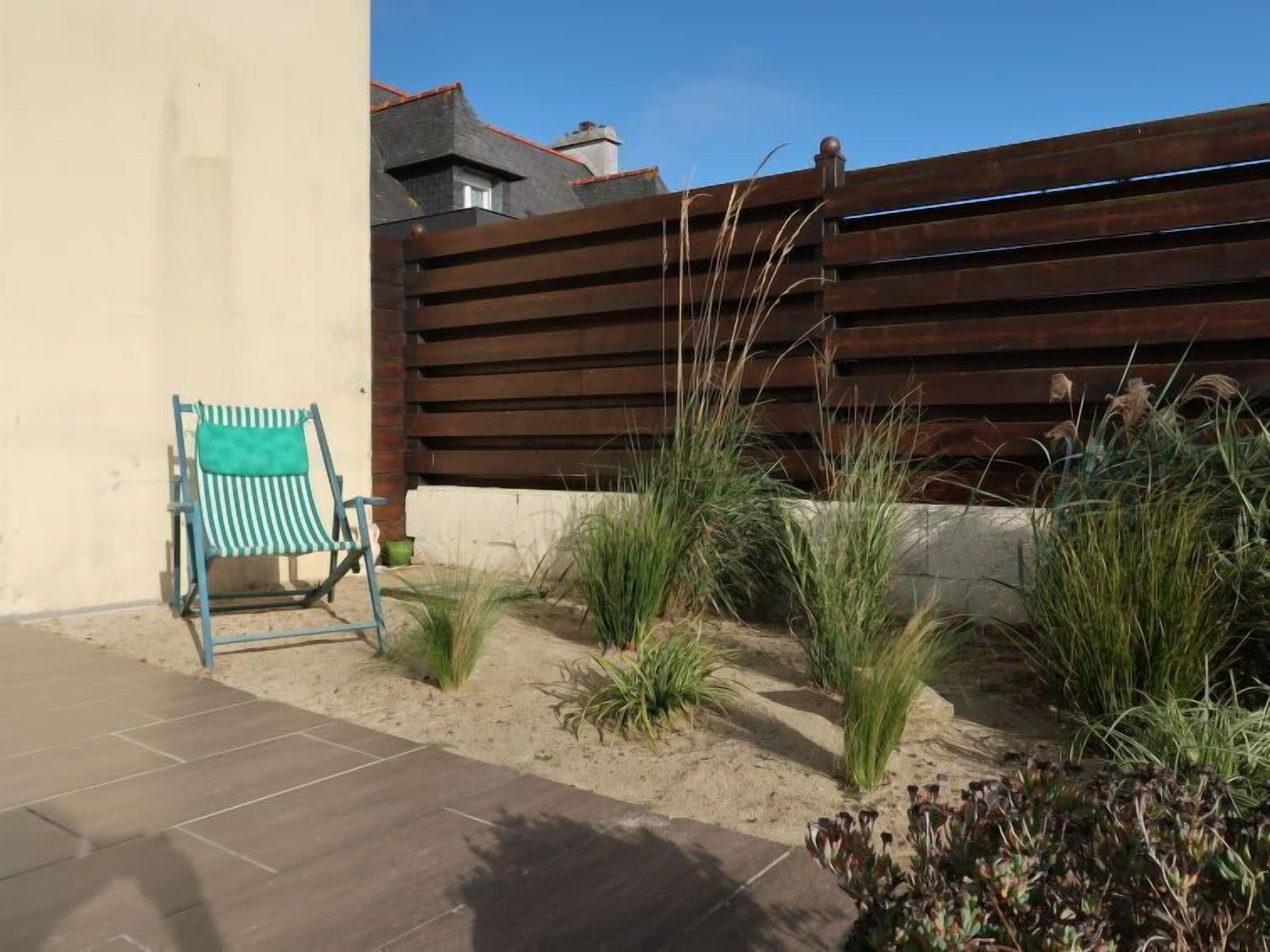 Un'area patio con una sedia a righe, una recinzione in legno e diverse piante.