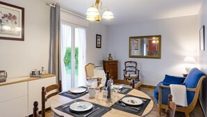 A dining area with a round table set for four, a blue sofa, and a large window with curtains. - Les Dunes by Interhome (Saint Pabu)