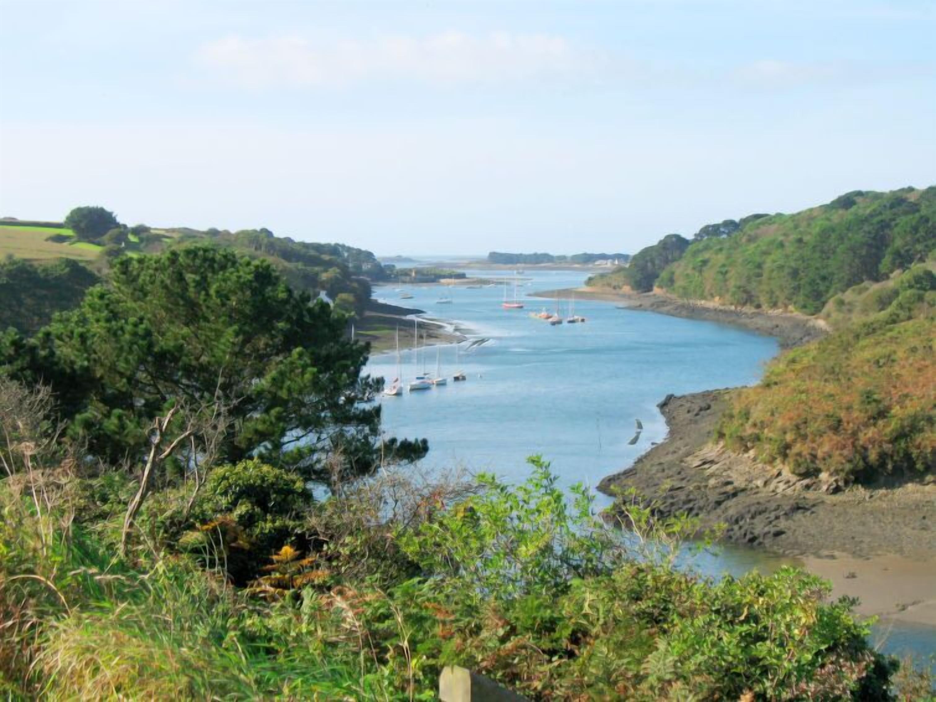 A coastal landscape with a river, boats, and greenery.