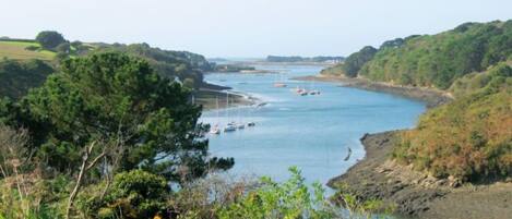 A coastal landscape with a river, boats, and greenery.