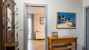 A hallway with a wooden cabinet, a table with a glass container, and a painting of a beach scene. - Les Dunes by Interhome (Saint Pabu)