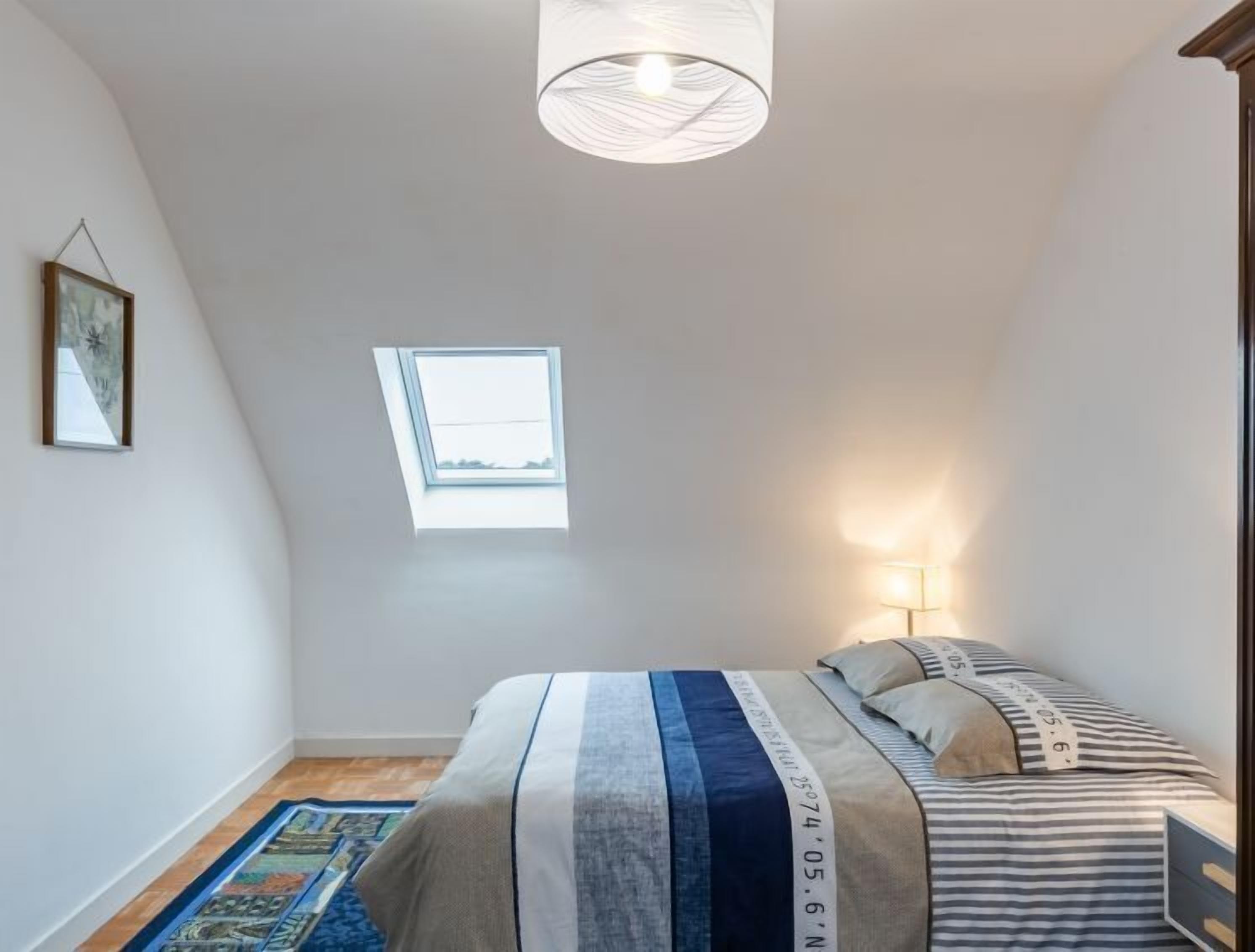 Et soveværelse med seng, vindue, lampe og loftlampe.