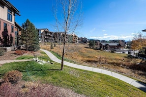 A residential area with a paved walkway, a tree, and buildings in the background.
