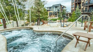 Un espace avec un jacuzzi, une terrasse en bois, des chaises longues et une piscine.