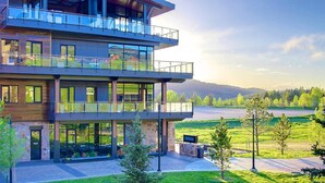 Un immeuble à plusieurs étages doté d’une façade en verre, d’une terrasse et offrant une vue sur un lac et des collines.