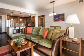 A modern living room with a green sofa, wooden coffee table, and a dining area in the background.