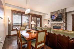 A modern living room with a wooden dining table, green cushioned seating, and a stone fireplace. - June Dates Just Opened at Great Rates! Pool/Hot Tub (Steamboat Springs)