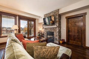 A living room with a stone fireplace, a television mounted on the wall, and a large wooden door.