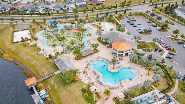 An aerial view of a resort with multiple swimming pools, a dock, and a parking area.