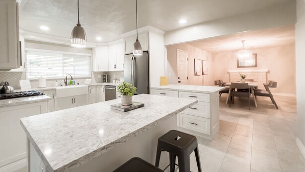 A modern kitchen with white cabinetry, a marble island, and a dining area with a table and chairs. - Home near Calistoga w/ heated pool & hot tub (Santa Rosa)