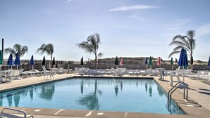 A pool area with lounge chairs and umbrellas, surrounded by a stone wall and palm trees. - Pool, Trail Access! Dog-Friendly Ocean Pines Haven (Ocean Pines)