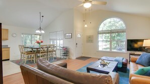 A spacious living room with a brown leather couch, a coffee table, and a TV. There is a dining area with a table and chairs, and a large window providing natural light. - Pool, Trail Access! Dog-Friendly Ocean Pines Haven (Ocean Pines)