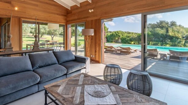 A modern living room with a sofa, coffee table, and large windows overlooking a pool and garden. - Villa Lavezzi by Interhome (Bonifacio)