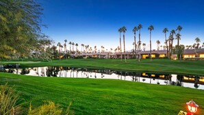 Ein Golfplatz mit Teich, der die Gebäude spiegelt, umgeben von Palmen und gepflegtem Rasen.