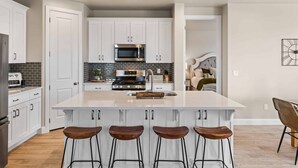 A modern kitchen with white cabinets, a central island with stools, a microwave, and a stove. - The Jungalow by RedAwning (Washington)