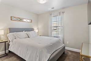 A bedroom with a bed, bedside tables, a nightstand, a window with blinds, and a wall-mounted light fixture. - Sunshine Seekers by RedAwning (Washington)