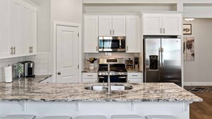 Una cocina moderna con armarios blancos, un refrigerador de acero inoxidable, microondas integrado y encimera de granito.