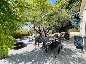 An outdoor patio with a dining table and chairs, surrounded by greenery and a building.