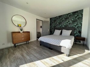 Quarto moderno com cama, penteadeira, espelho e parede estampada.