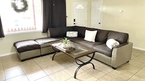 Un salon avec un canapé d’angle, une table basse et une fenêtre avec des rideaux.