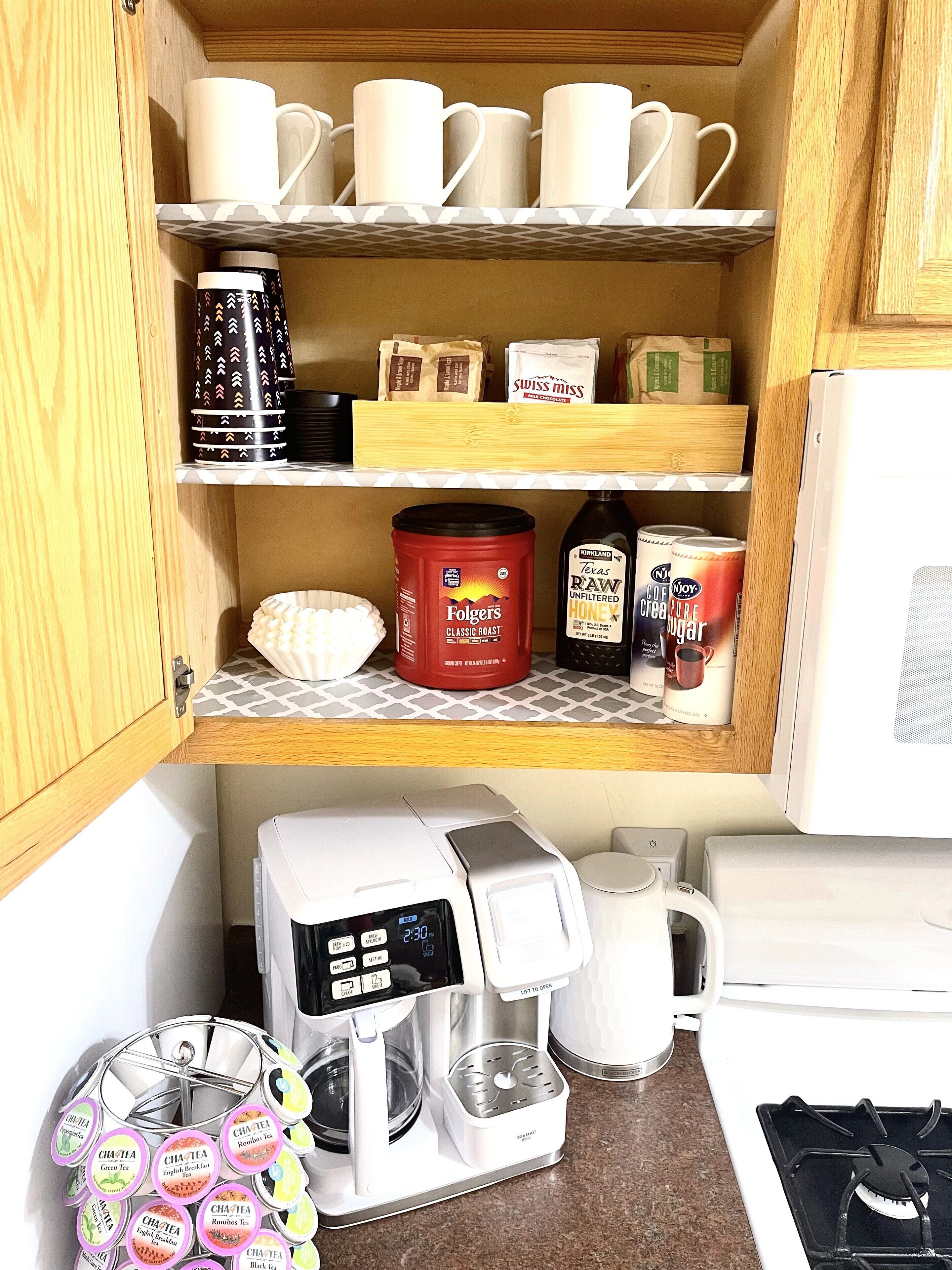 A kitchen with a coffee maker, a microwave, and shelves with coffee cups, coffee beans, and a canister.