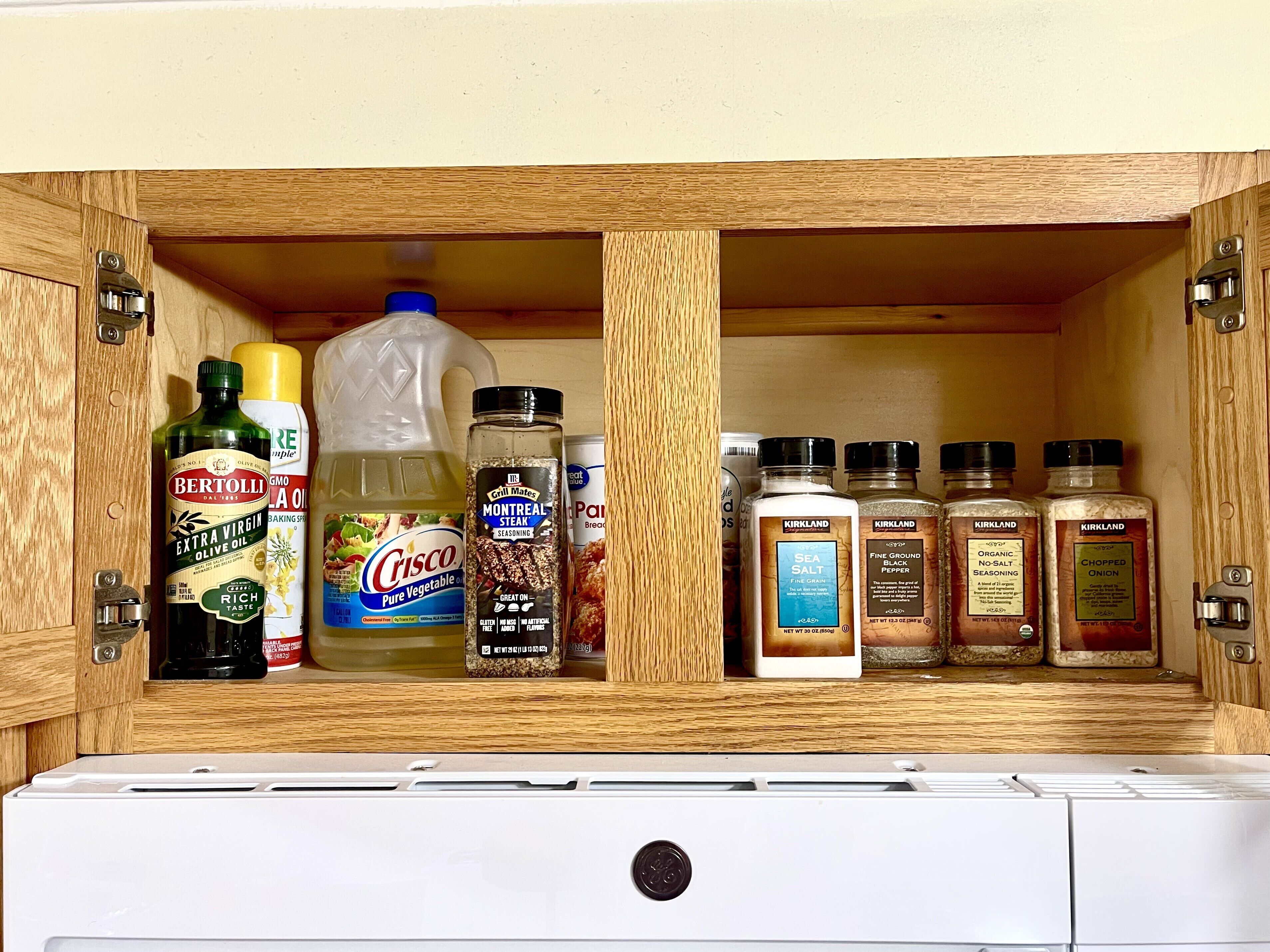 Ein Küchenschrank mit verschiedenen Lebensmitteln, darunter natives Olivenöl, Pflanzenöl, Gewürzen und Salz.