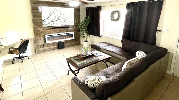 Un salon comprenant un canapé, une table basse, une cheminée, un ventilateur de plafond et un téléviseur fixé au mur.