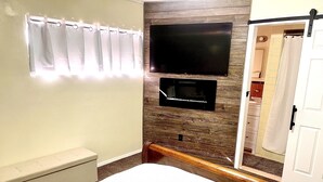 Une chambre à coucher comprenant un lit, un téléviseur fixé au mur (qui est en bois), une douche et des toilettes.