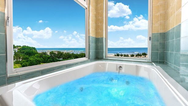 A large bathtub with a clear view of a beach and ocean through a large window. - Hi Yeongjin Spa Pension (Gangneung)