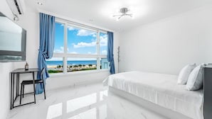 A modern bedroom with a large window offering a beach view, a bed with white linens, a small table with a bottle, and a chair. - Hi Yeongjin Spa Pension (Gangneung)