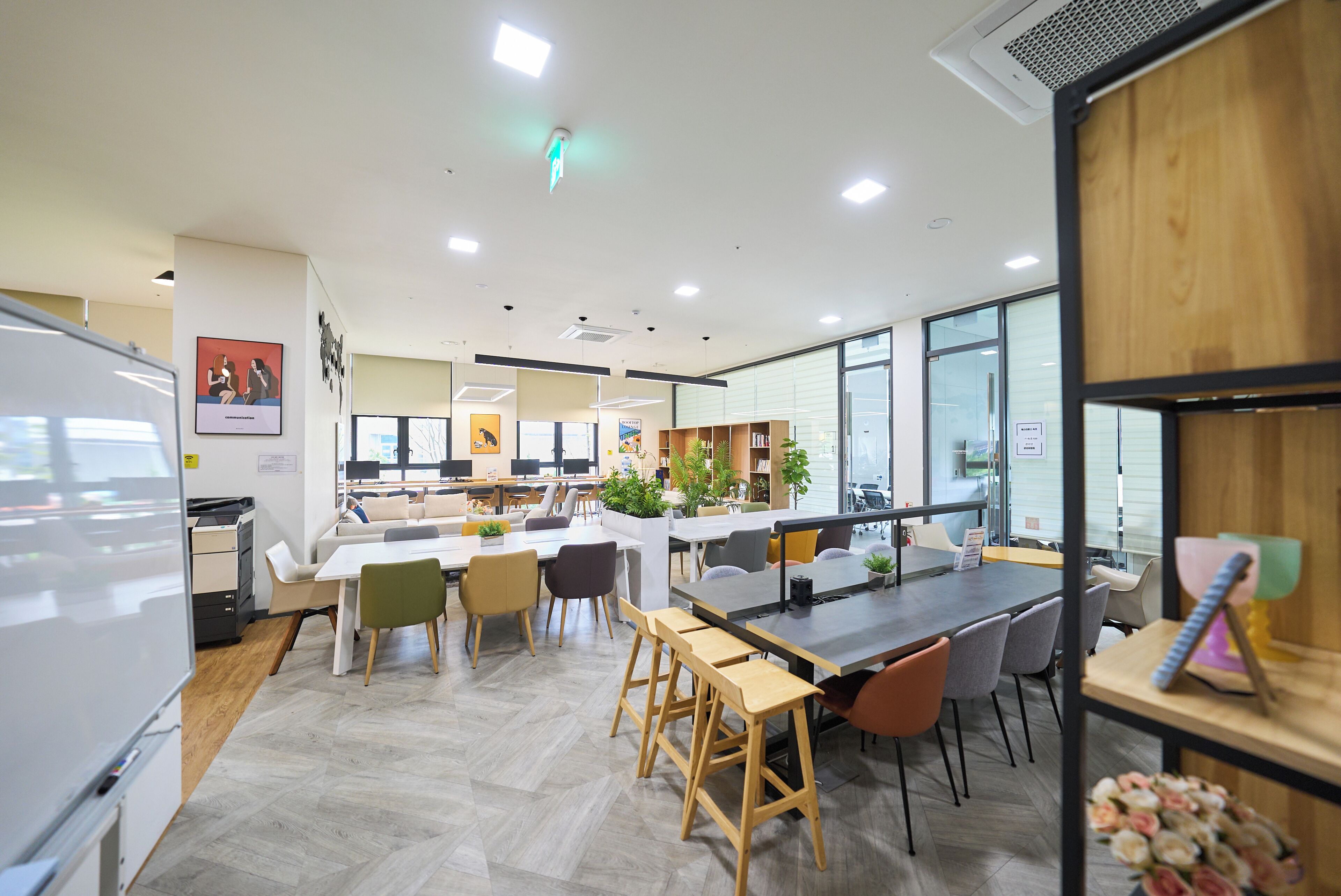 A modern office space with a central island table, multiple seating areas, and large windows.