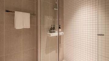 Un baño con cabina de ducha de vidrio, un perchero con dos toallas, un dispensador de jabón y un pequeño estante con artículos de aseo.