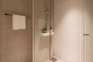Un baño con cabina de ducha de vidrio, un perchero con dos toallas, un dispensador de jabón y un pequeño estante con artículos de aseo.
