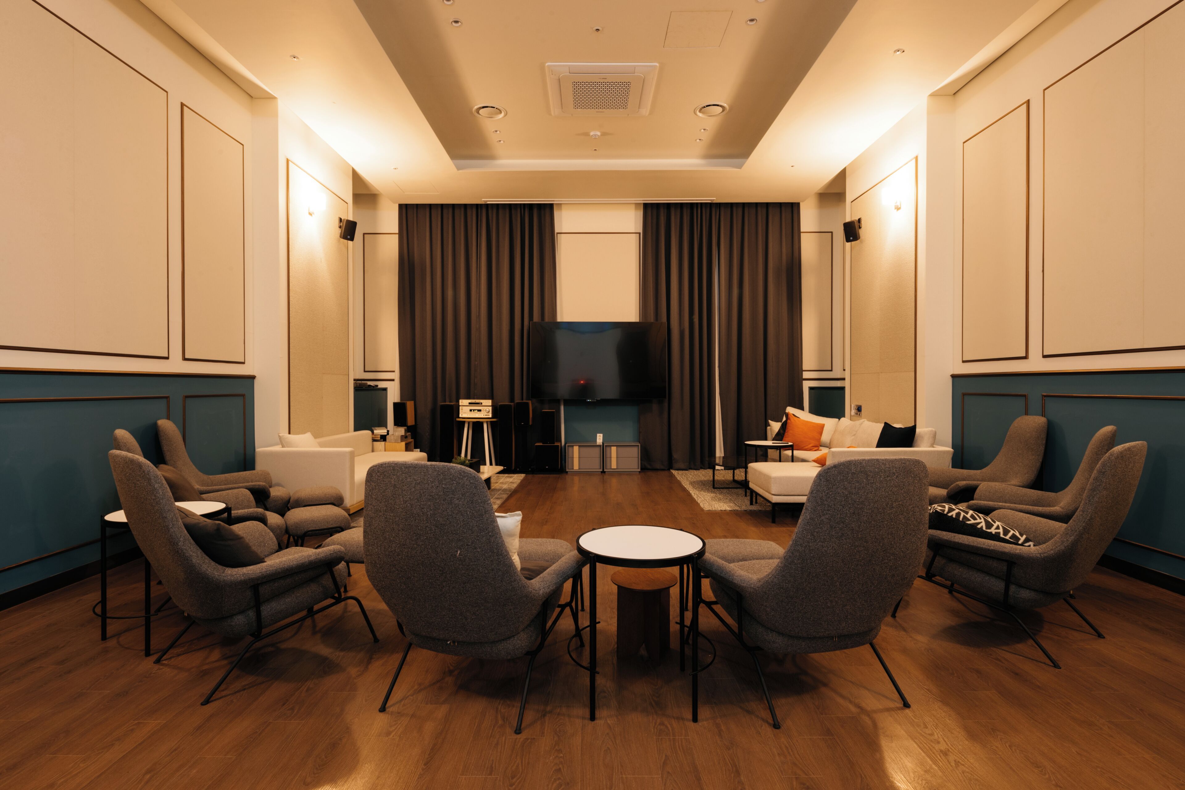 A modern hotel room with a wooden floor, a flat-screen TV, a sofa, armchairs, and a small round table.
