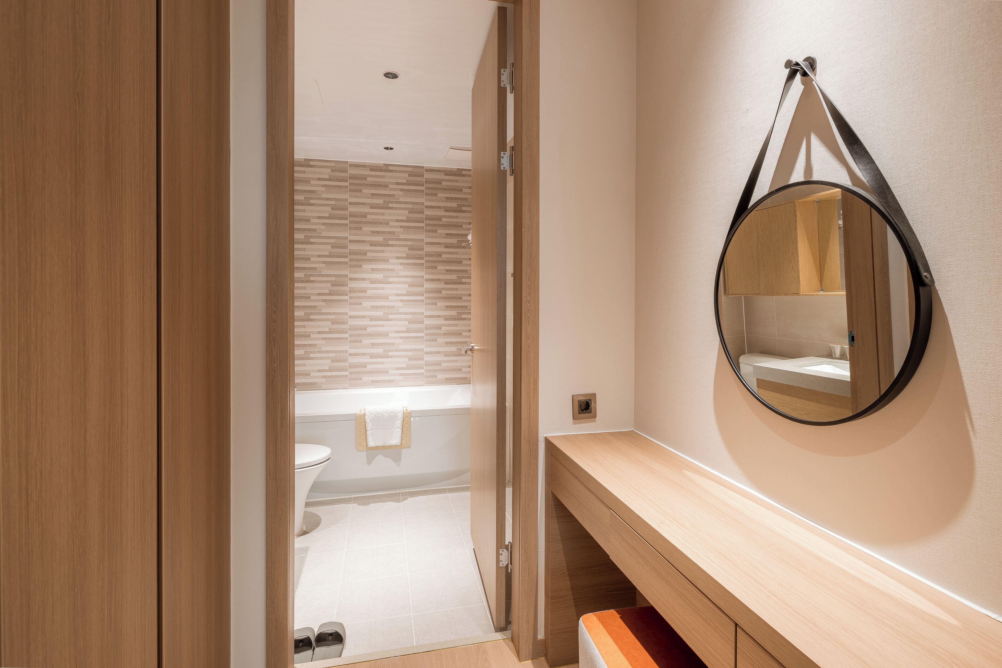 A modern bathroom with a wooden vanity, a round mirror, and a visible shower area.