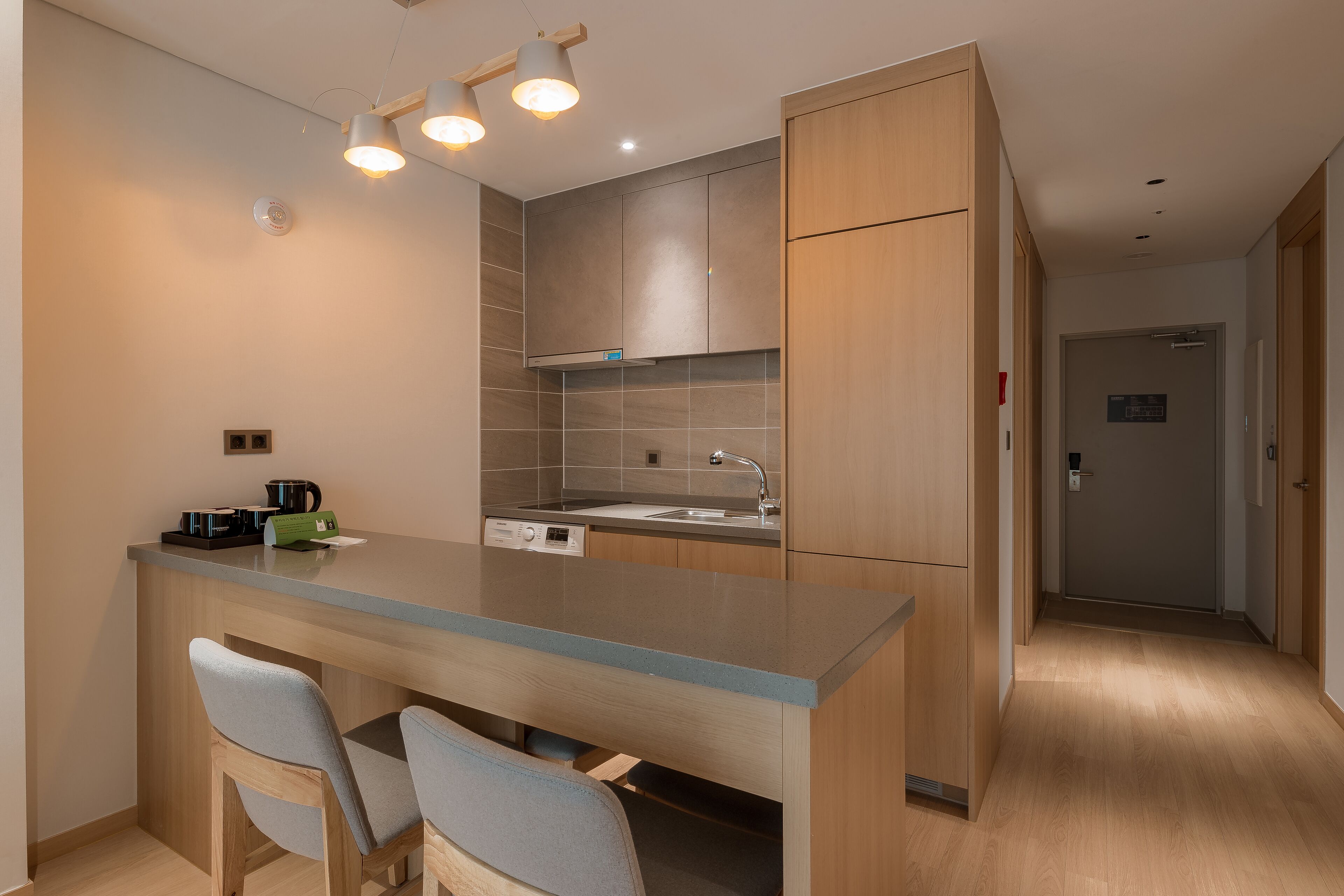 Cocina moderna con una isla central, dos taburetes de bar, armarios de madera y un lavamanos de acero inoxidable.