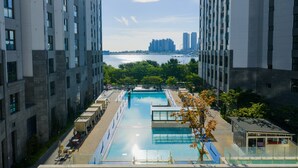 Un edificio de gran altura con piscina, varios balcones y vistas a un horizonte urbano sobre un cuerpo de agua.