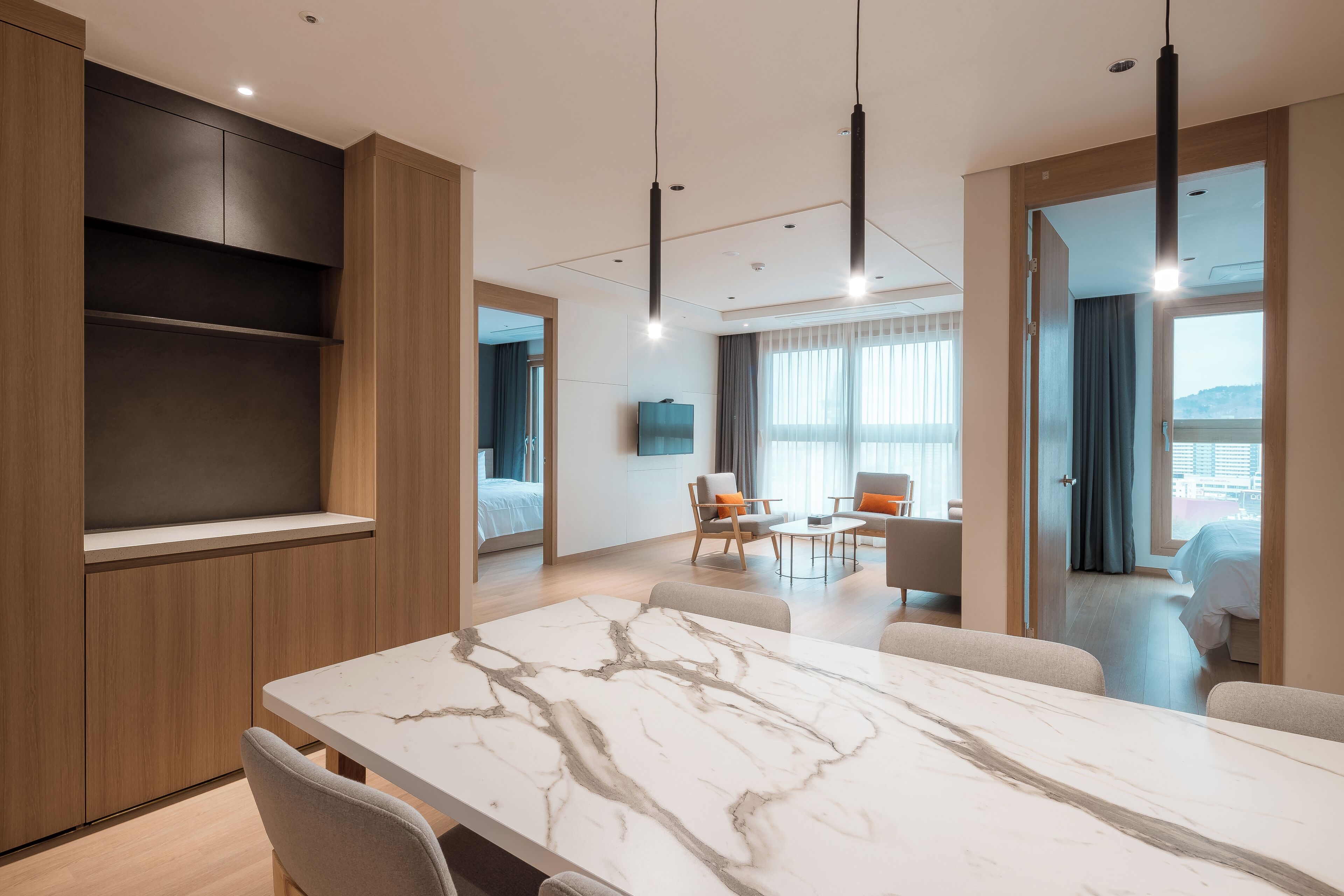 Una habitación de hotel moderna con una mesa de comedor de mármol, un sofá, un televisor y un balcón con vistas.
