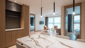 Una habitación de hotel moderna con una mesa de comedor de mármol, un sofá, un televisor y un balcón con vistas.