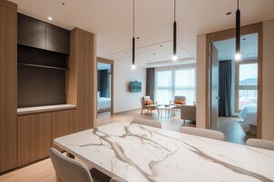 Una habitación de hotel moderna con una mesa de comedor de mármol, un sofá, un televisor y un balcón con vistas.