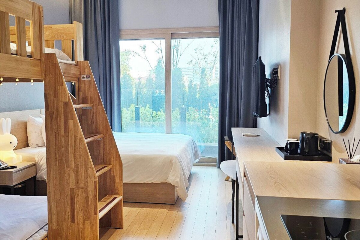 Habitación de hotel con literas, un escritorio con espejo, teléfono y vistas a zonas verdes.