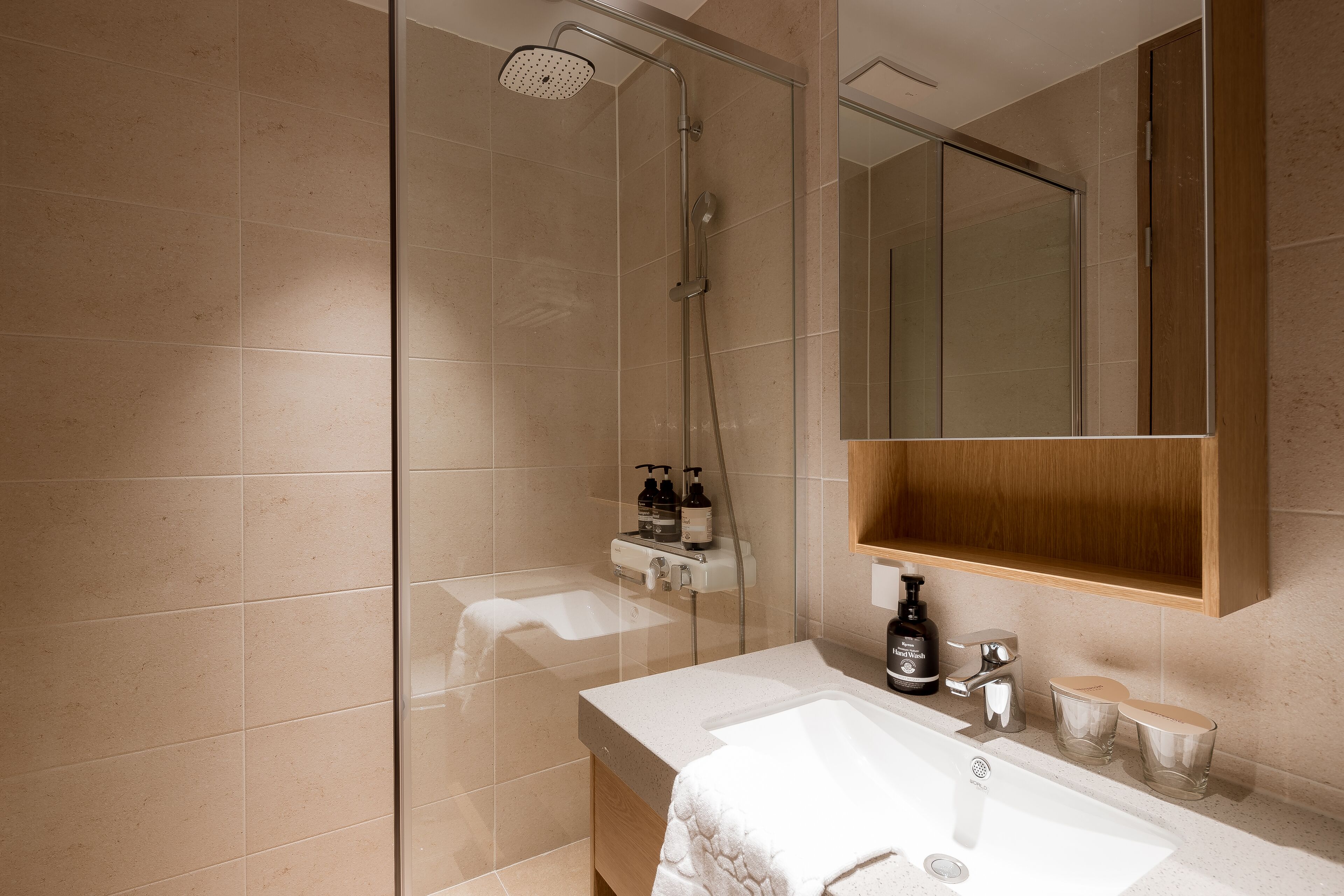 A modern bathroom with a glass-enclosed shower, a white sink, and a wooden vanity.