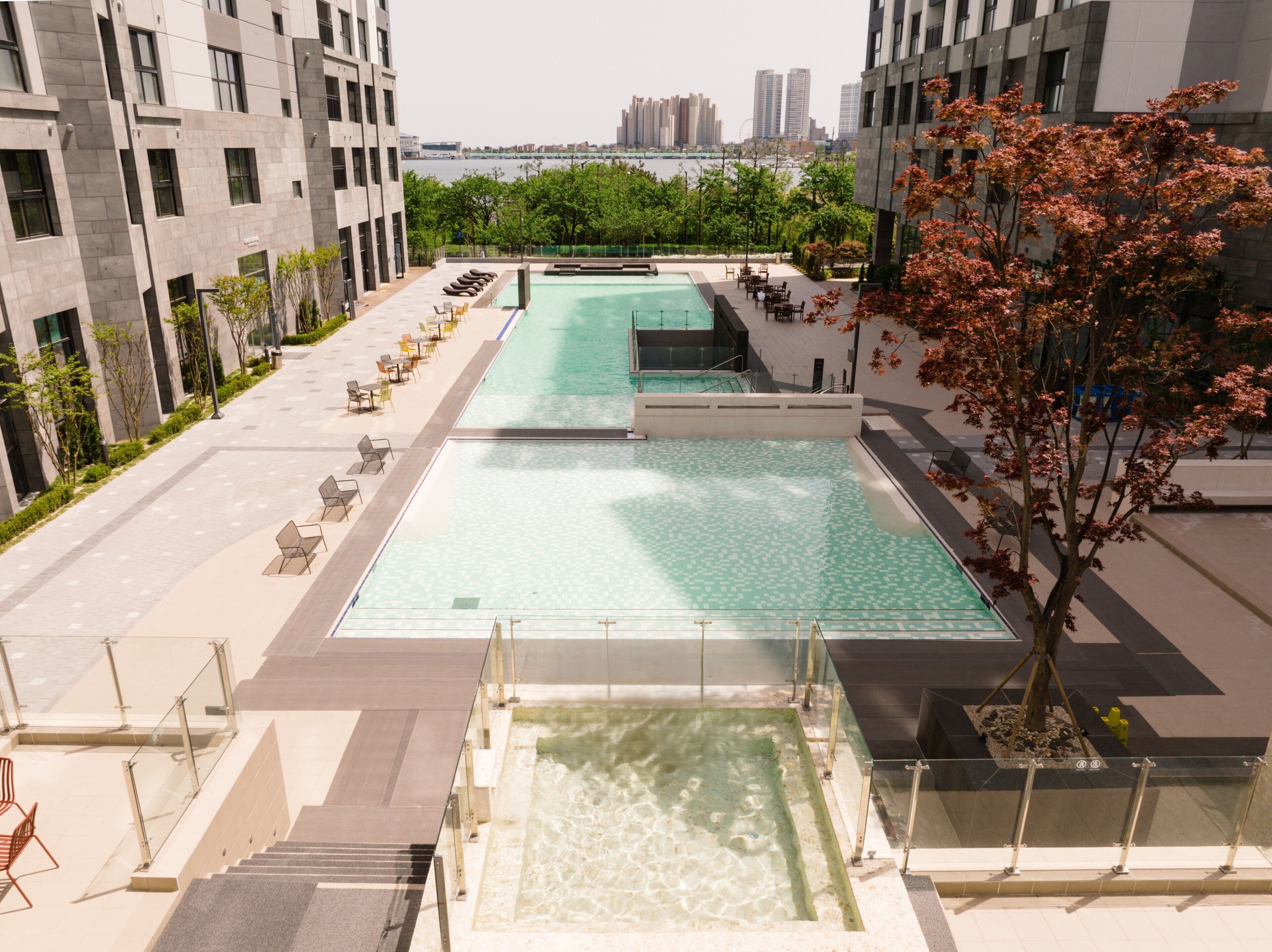 A rooftop swimming pool with a view of a city skyline, surrounded by modern buildings and trees.
