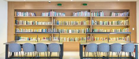 Uma biblioteca com várias estantes, duas mesas com cadeiras e um teto com iluminação embutida.