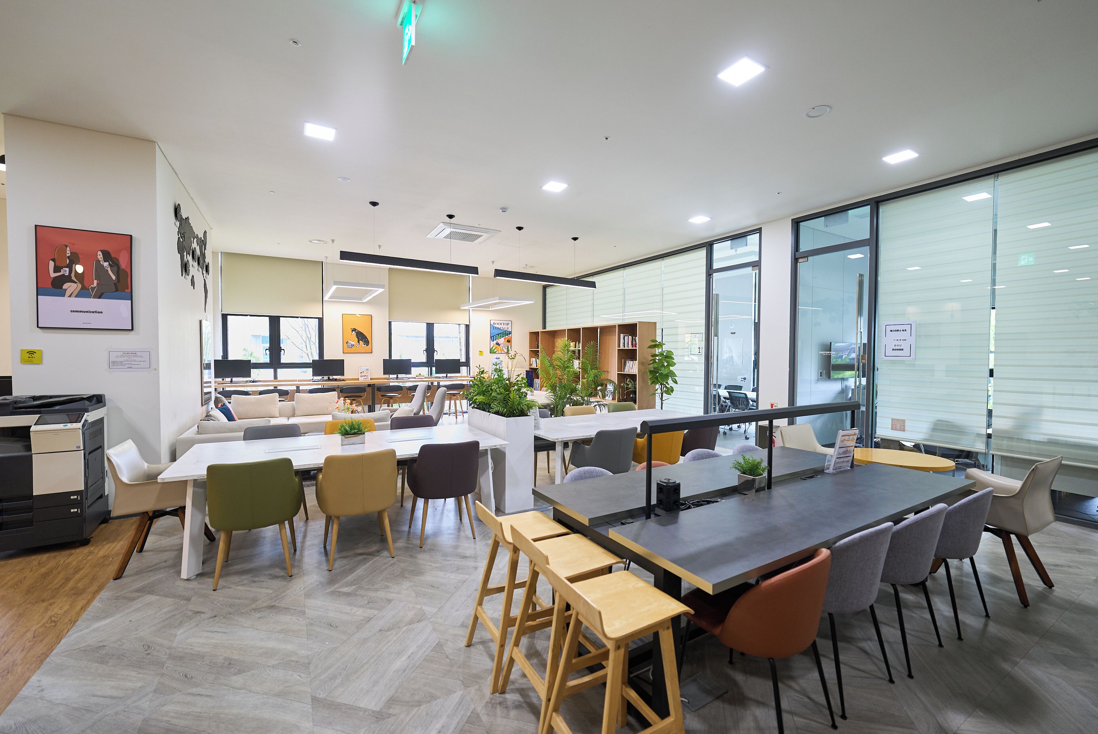 A modern office space with a long table, multiple chairs, and a bookshelf.