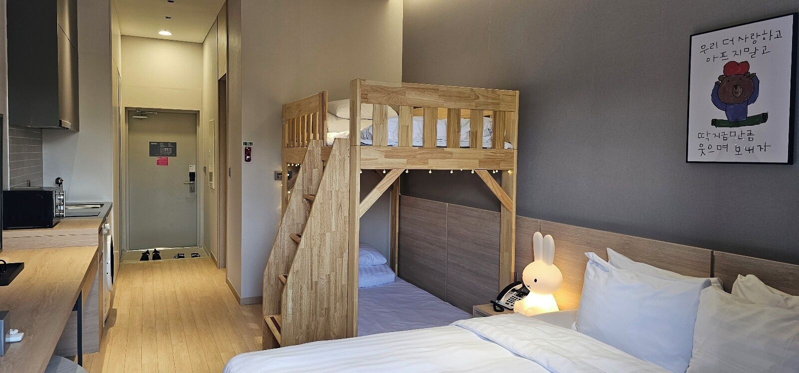 A hotel room with a bunk bed, a bedside table, a lamp, and a wall-mounted artwork.
